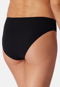Perizoma nero a coste con copertura media, vita senza cuciture e texture liscia. Design della parte posteriore curva per un aspetto aderente.
