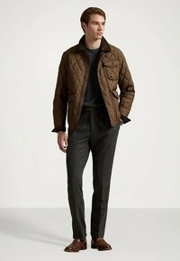 Καφέ επενδυμένο μπουφάν με ψηλό γιακά, μπροστά τσέπη και κουμπιά σνάπ, σε συνδυασμό με γκρι μάλλινες παντελόνες και καφέ δερμάτινα παπούτσια.