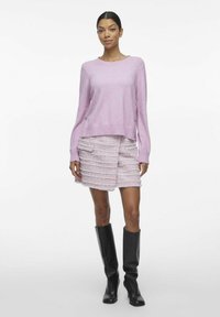 Jasnoróżowy, krótki sweter z długimi rękawami i ściągaczem na dole, zestawiony z falbaniastej spódnicy w nieco ciemniejszym odcieniu różu oraz czarnymi kozakami za kolano.