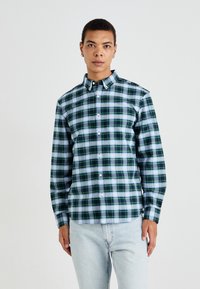 Groen en blauw geruite overhemden met kraag, voorzien van lange mouwen en witte knopen. Draag met lichtblauwe jeans.