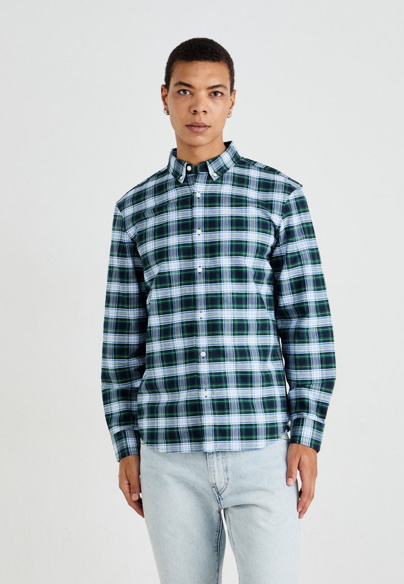 Groen en blauw geruite overhemden met kraag, voorzien van lange mouwen en witte knopen. Draag met lichtblauwe jeans.
