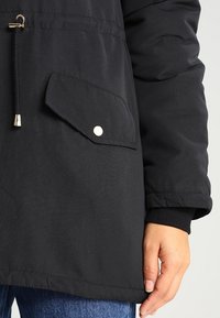 Czarna ocieplana kurtka z ściągaczem w talii, z ukośną kieszenią na klatce piersiowej zapinaną na napę, oraz prążkowanymi mankietami. Widoczny detal z teksturowanej tkaniny.