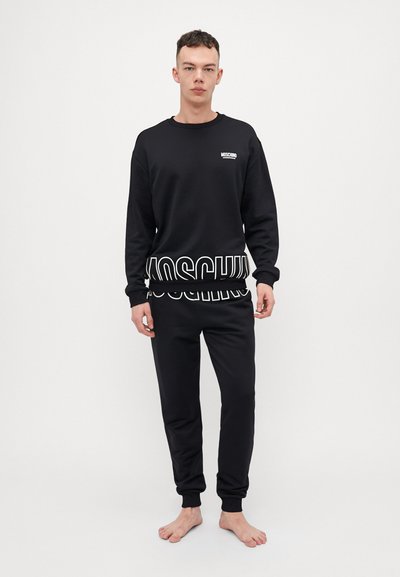 Black sweatshirt and sweatpants set featuring a Moschino logo in white at the waist and chest, with ribbed cuffs and a soft texture.