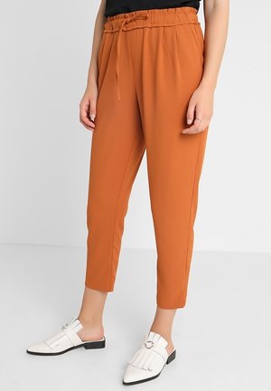 Mujer vistiendo pantalones cortos de color óxido con cintura elástica y mocasines blancos sin cordones con detalles de flecos sobre un fondo blanco.