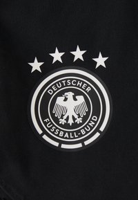 Μαύρος ύφασμα με κυκλικό λογότυπο που απεικονίζει ένα λευκό αετό, τέσσερις λευκούς αστέρες από πάνω και το κείμενο "DEUTSCHER FUSSBALL-BUND" γύρω από τον αετό.