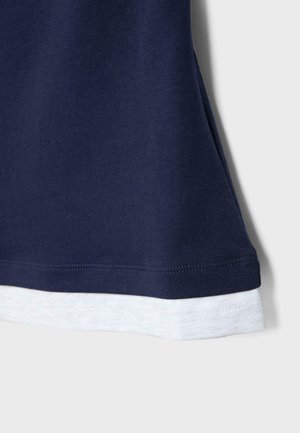 Tessuto blu navy sovrapposto a tessuto grigio chiaro con cuciture visibili ai bordi, che mostra parte dell'orlo di un indumento.