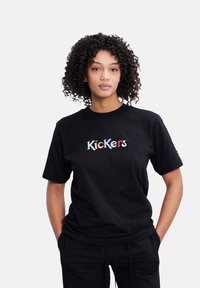 Camiseta negra de algodón, con el logo bordado de "Kickers" en texto multicolor. Cuello redondo y mangas cortas.