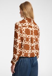 Bruine en crème gearceerde shirt, met lange mouwen, een rechte snit en een rugplooi. Gemaakt van lichtgewicht, soepel materiaal.