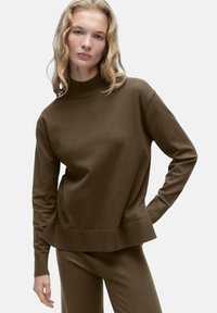 Rjav pulover s visokim ovratnikom, dolgimi rokavi in sproščenim krojem. Narejen iz mehkega, teksturiranega blaga z rebrastim robom.