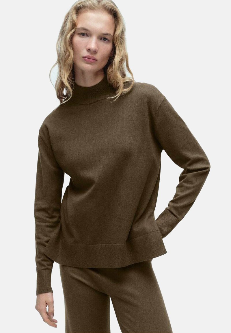 Rjav pulover s visokim ovratnikom, dolgimi rokavi in sproščenim krojem. Narejen iz mehkega, teksturiranega blaga z rebrastim robom.