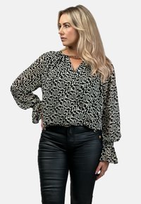 Czarna i biała bluzka w abstrakcyjny wzór z długimi rękawami i dekoltem w kształcie litery V, połączona z spodniami z wysokim stanem z czarnej skóry.