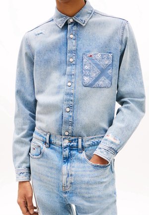 Lyseblå denimskjorte med metal knapper og mønstret brystlomme kombineret med matchende lyseblå denim jeans.