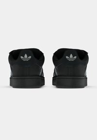 Μαύρα αθλητικά παπούτσια με λείο υλικό, που διαθέτουν τρεις λευκές ρίγες, επενδεδυμένο γιακά και λογότυπο στη φτέρνα. Επίπεδη σόλα από καουτσούκ.