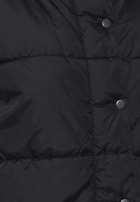 Černá prošívaná bunda s hladkým materiálem, charakterizovaná prošívaným designem, drukovými knoflíky a výraznými švy. Texturovaná a zateplená.