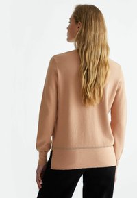 Maglione lavorato a maglia color pesca con tessuto testurizzato, maniche lunghe e un accento dorato all'orlo, caratterizzato da una vestibilità rilassata e spacco sui lati.