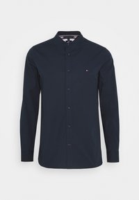 Maglietta a maniche lunghe blu navy con colletto alla coreana e chiusura con bottoni. Presenta un piccolo logo sul petto. Realizzata in tessuto liscio.