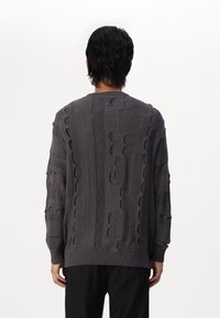 Szary dzianinowy sweter z fakturowanymi wzorami i ażurowymi detalami. Posiada ściągacze na rękawach i dole, okrągły dekolt oraz luźny fason.