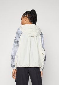 Lightweight jacket in beige and gray with a marbled pattern on the sleeves, featuring a hood and elastic cuffs for a fitted look.