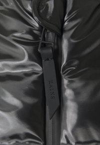 Svart vadderad jacka med en glansig yta, med en central dragkedja och en tygetikett med ordet "RAINS" präglat.