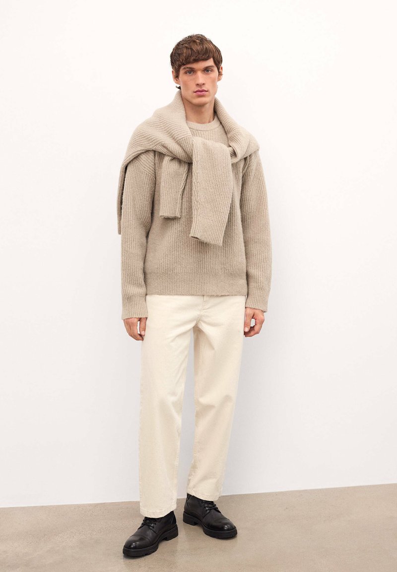 Beeži ribaga kootud sviiter, seljas, koos kreemjatest pükstest ja mustadest laces-up kingadest. Sile tekstuur ja lõdva lõikega.