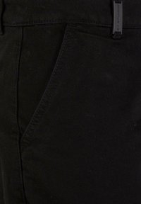 Pantalons en coton noirs avec une coupe slim, une poche latérale et une texture subtile avec des coutures ton sur ton et une étiquette de ceinture de marque.