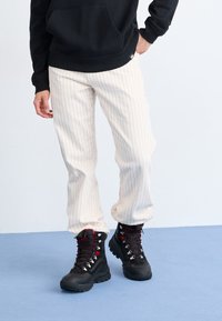 Lyse creme stribede bukser med en afslappet pasform, parret med sorte vandrestøvler med røde snørebånd og metaløjer. Sort sweatshirt ovenfor.