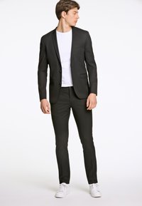 Schwarzer maßgeschneiderter Blazer mit einem Knopf, kombiniert mit schmal geschnittenen schwarzen Hosen und einem weißen Hemd. Legere weiße Sneakers runden den Look ab.