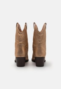 Bronze cowboy boots with embroidered wing patterns, pointed toe, low stacked heel, and pull tabs on the sides. Smooth, metallic finish.