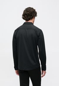 Zwart shirt met lange mouwen, gladde textuur, klassieke kraag en knoopmanchetten. Heeft een afgeronde zoom en een minimalistisch ontwerp.