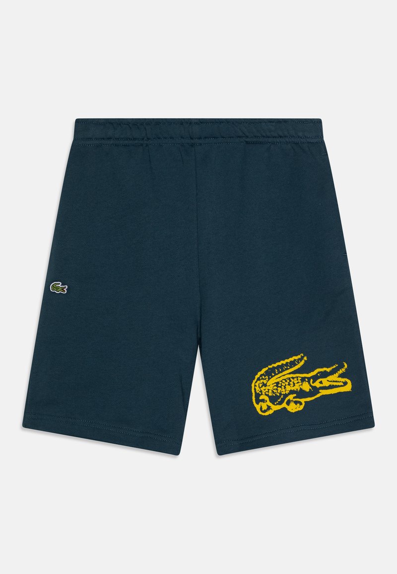 Merimekko siniset puuvillahousut, joissa on joustava vyötärö ja suuri keltainen krokotiilikuva oikealla lahkeella. Sisältää pienen logotägin.