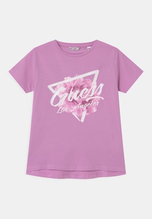 Lavendelfarbenes T-Shirt mit kurzen Ärmeln und weißem "Guess Los Angeles" Schriftzug über einem pinken Blumen- und Dreiecksmotiv auf der Vorderseite.