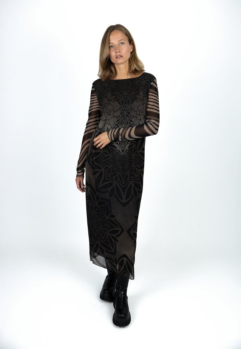 Langes schwarzes Kleid mit transparenten langen Ärmeln, verziert mit floralen und geometrischen Mustern, getragen mit schwarzen klobigen Stiefeln. Glatte Textur, elegantes Design.
