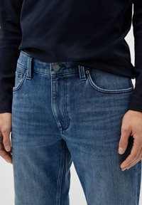 Jeans aus Denim in einer mittleren blauen Farbe, mit einem klassischen Fünf-Taschen-Design, Metallknopfverschluss und subtiler Verwaschung des Stoffes.