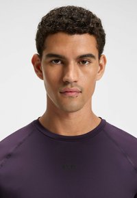 Purple athletic shirt with a round neckline, featuring subtle shoulder seams and a small black "BOSS" logo on the chest. Smooth texture.