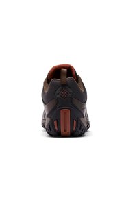 Zapatilla deportiva marrón y negra vista desde atrás, con una suela texturizada y una tira en el collar del talón.