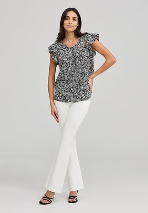 Blusa floreale in bianco e nero con maniche a rouches, abbinata a pantaloni bianchi a campana e sandali neri con cinturini. Texture liscia, design casual.
