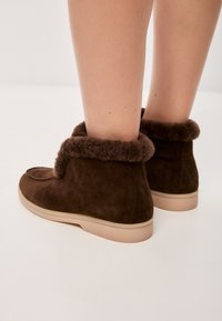 Bottines en daim marron avec une bordure douce ressemblant à de la fourrure, semelles en caoutchouc et une conception à bout arrondi. Des détails de couture minimalistes sont visibles.