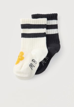 Dva páry rebrovaných ponožiek po členky, jeden biely s čiernymi pruhmi a žltým detailom, druhý čierny s bielymi pruhmi, prekrývajúce sa.