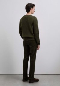 Suéter de canalé verde oscuro y pantalones de pana a juego. El conjunto tiene un corte relajado, con textura visible y detalles suaves en los zapatos.