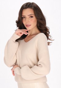 Maglione beige a coste con scollatura a V, maniche oversize e finitura texture. Il tessuto appare soffice e comodo, adatto per un look casual.