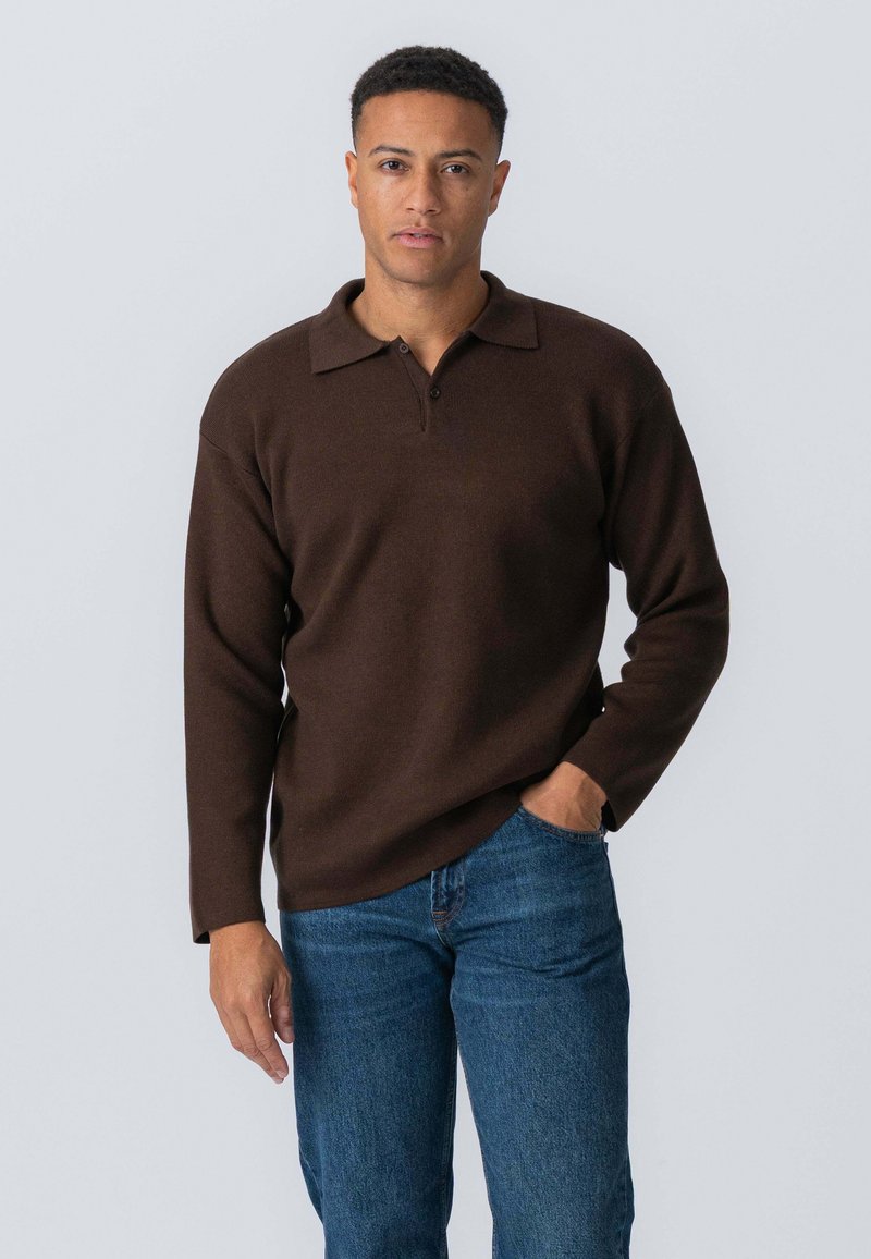 Brun pullovertrøje med klassisk krave og lange ærmer, lavet af blødt materiale. Bæres med blå jeans, hænderne ned langs siden.