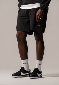 Pantaloni corti leggeri neri con vita elasticizzata e tasche laterali, abbinati a sneaker nere Nike con dettagli bianchi e calze bianche.