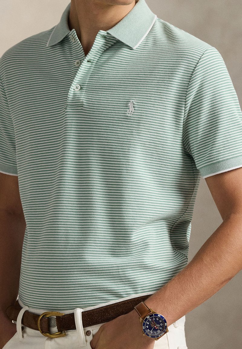Light green and white striped polo shirt with a three-button placket and a small embroidered logo. Worn with a brown belt and watch.