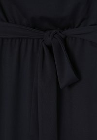 Tissu bleu marine foncé avec une texture lisse, présentant un détail de ceinture nouée à la taille à l'avant, créant un effet froncé sur le vêtement.