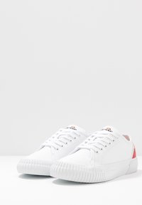 Sneakers bianchi in tela con suole in gomma, punta rotonda, design con lacci e logo multicolore sulla linguetta. Presentano accenti laterali color corallo.