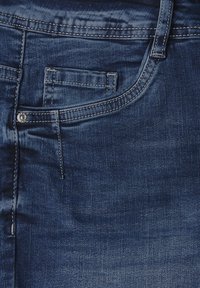 Jeans en denim bleu foncé avec une poche avant, des coutures visibles et un détail de bouton en métal. Texture lisse avec de légères marques d'usure.