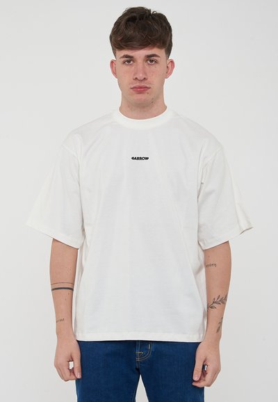 T-shirt blanc à manches courtes en tissu coton avec une coupe décontractée. Présente un logo noir imprimé sur la poitrine. Associé à un jean bleu.