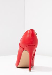 Zapato de tacón alto de cuero rojo con punta puntiaguda y tacón estrecho. Presenta un acabado texturizado y un cierre de cremallera en la parte trasera.