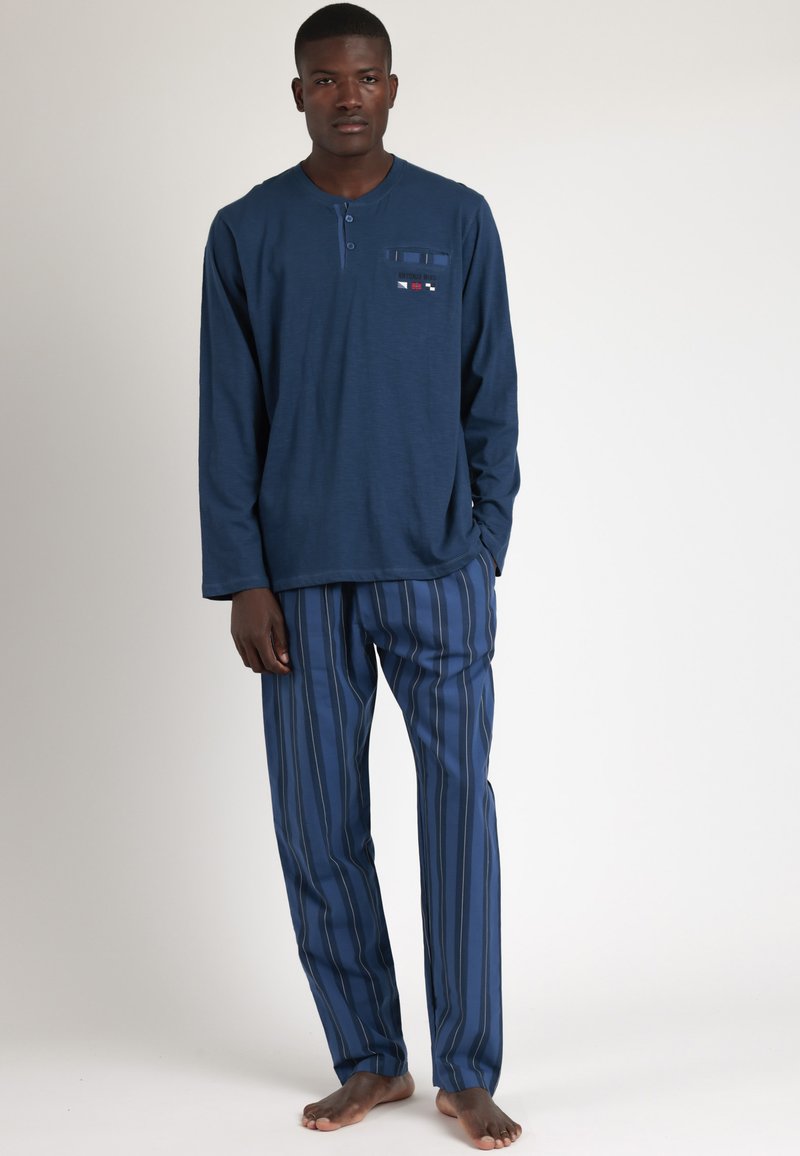 Camisa de manga larga en color navy con tapeta de botones y bolsillo en el pecho; pantalones de pijama a rayas en tonos a juego; tela suave, corte relajado.