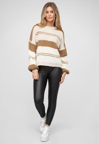 Strickpullover in creme- und braun gestreift, oversized Passform mit Ballonärmeln, kombiniert mit schwarzen Leggings und weißen Sneakers. Glatte Textur.
